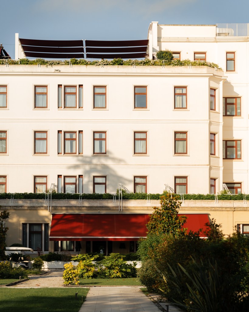 Exterior of the JW Marriott Venice hotel on the Grand Canal: pale stucco walls, wrought-iron balconies, and a red canvas awning above the waterside entrance