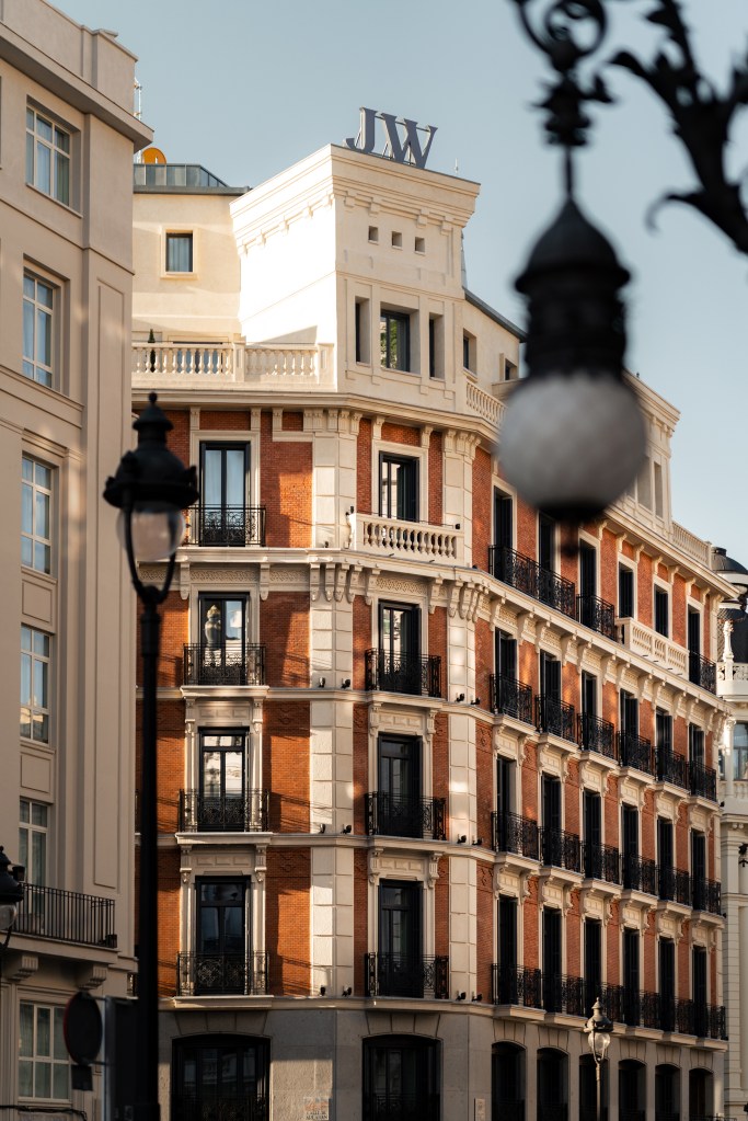 Sunlit exterior of JW Marriott Hotel Madrid: ornate stone balconies and classical architectural details bathed in warm morning light