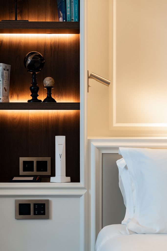 Cream-painted Sofitel Barcelona hotel bedside panel with built-in reading light, integrated power and USB outlets, and a white Philips air purifier standing next to crisp white bed linens