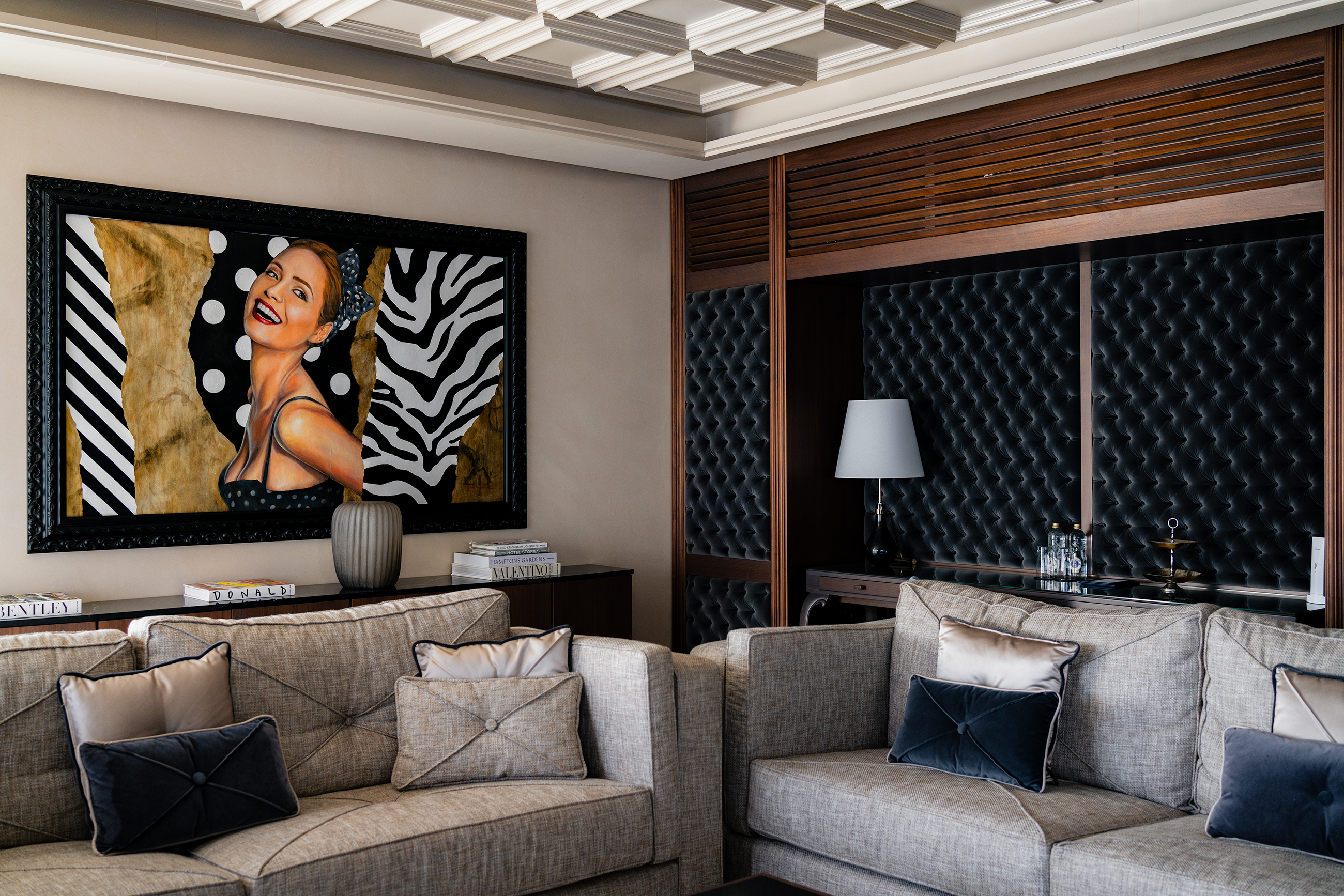 Sofitel Barcelona presidential suite living room with paired grey sofas, black marble coffee table, and framed pop-art painting beneath coffered ceiling