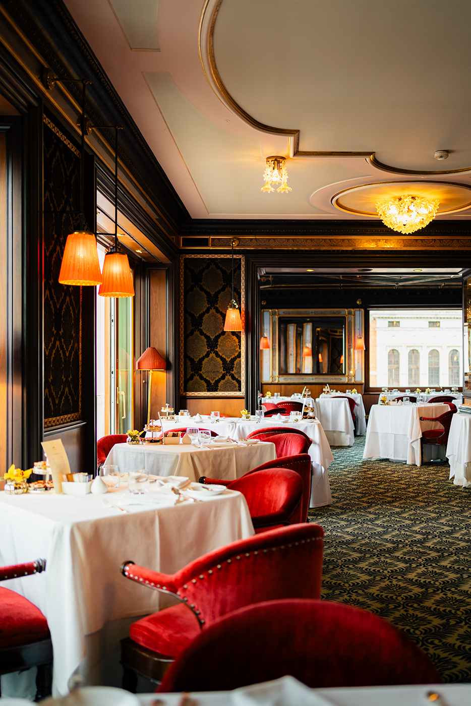 Refined dining room at Hotel Danieli in Venice with white tablecloths, red velvet chairs, warm pendant lighting, and mirrors reflecting the space