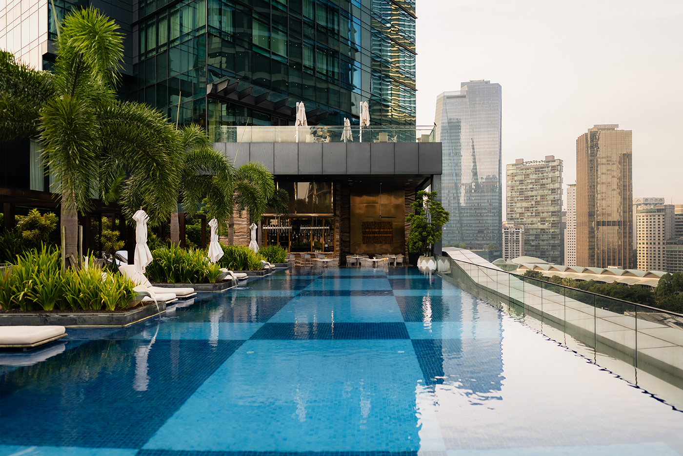 Four Seasons Kuala Lumpur rooftop infinity pool with lush landscaping, loungers, and the city skyline in the background