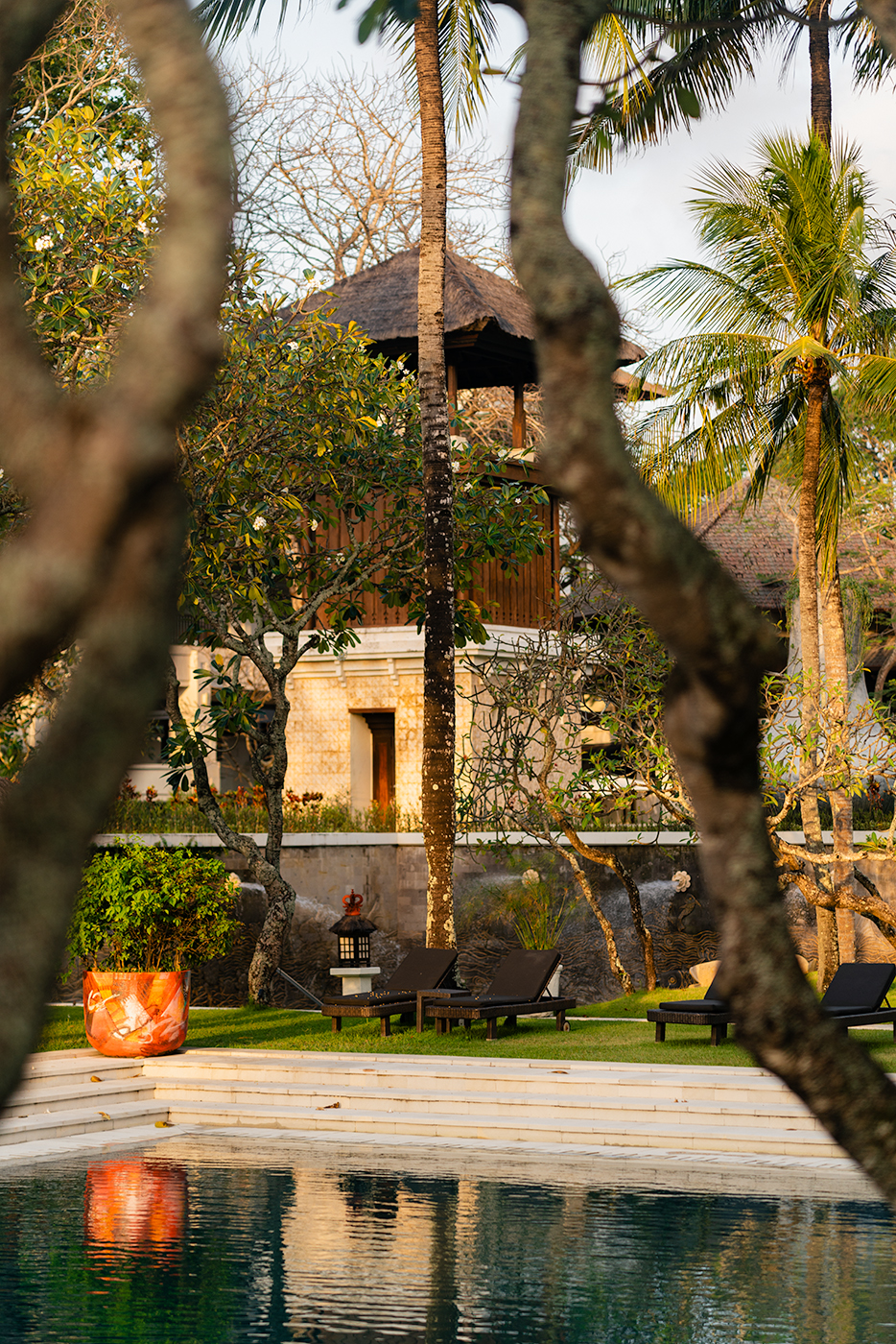 Poolside loungers and tropical greenery framing a traditional thatched-roof pavilion at golden hour, InterContinental Bali