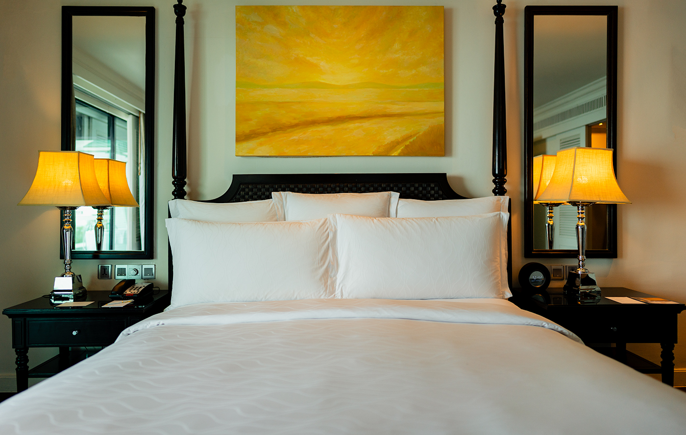 Symmetrical bedroom scene with a white king bed, twin bedside lamps, and artwork above the headboard, InterContinental Koh Samui.