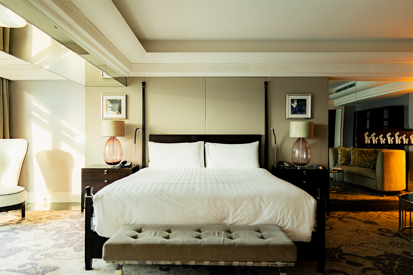 Centered king bed in a modern hotel room with glass bedside lamps and a lounge area in the background