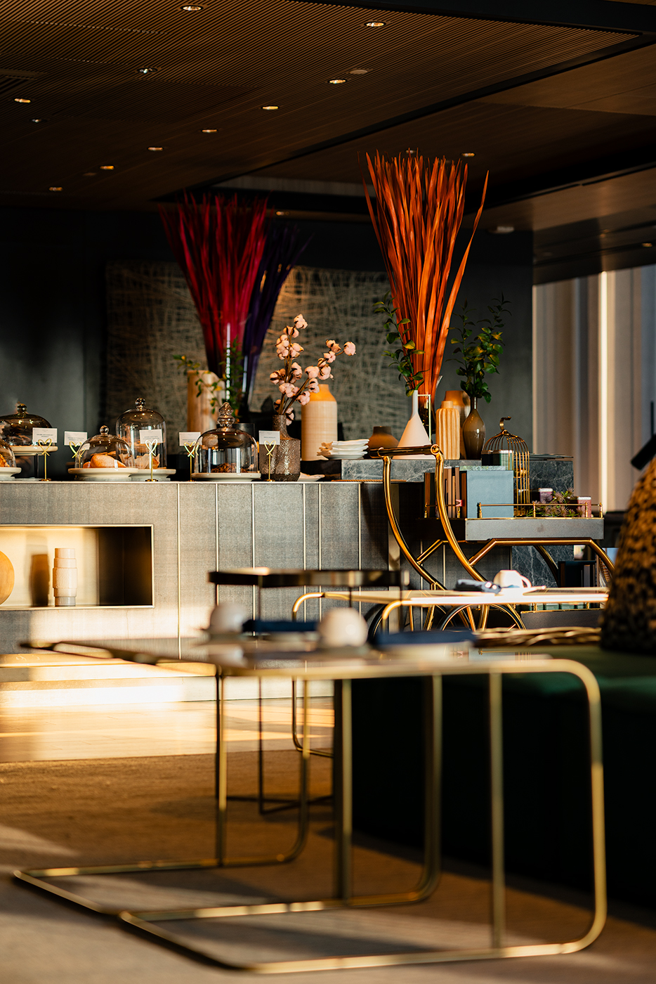 Breakfast lounge with buffet counter, glass cloches, sculptural vases, and a gold service cart in morning light, Kimpton.