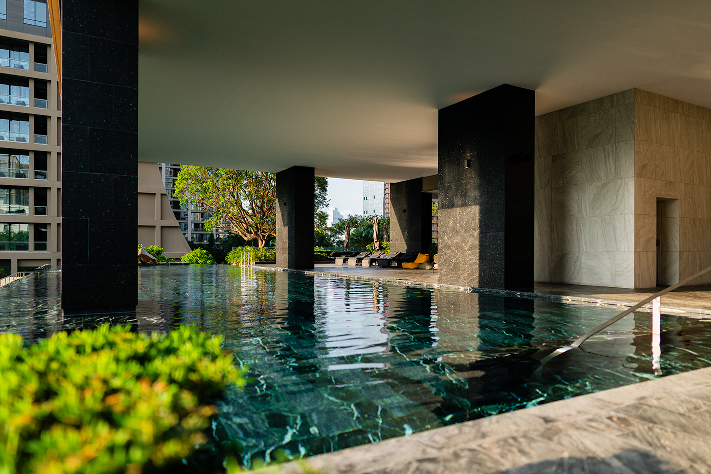Infinity-style pool under a large canopy with black columns, greenery in the foreground, and city buildings beyond, Kimpton.