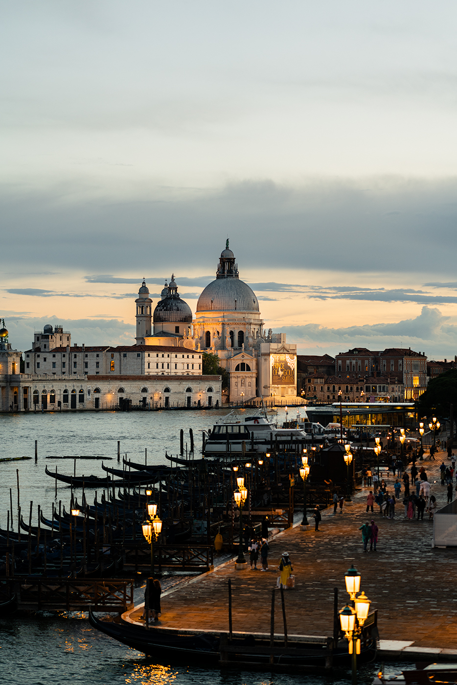 Evening view from Hotel Danieli over Venice’s waterfront, with gondolas lined along the promenade and Basilica Santa Maria della Salute glowing across the lagoon