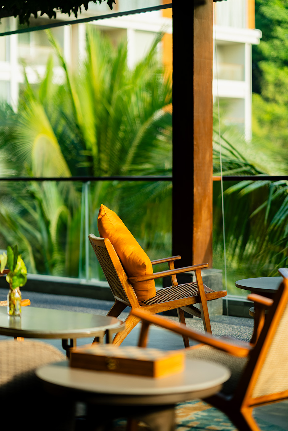 Warm, sunlit lounge scene at The Westin Resort & Spa Ubud, Bali, featuring a wooden armchair with an orange cushion beside floor-to-ceiling glass overlooking tropical greenery.