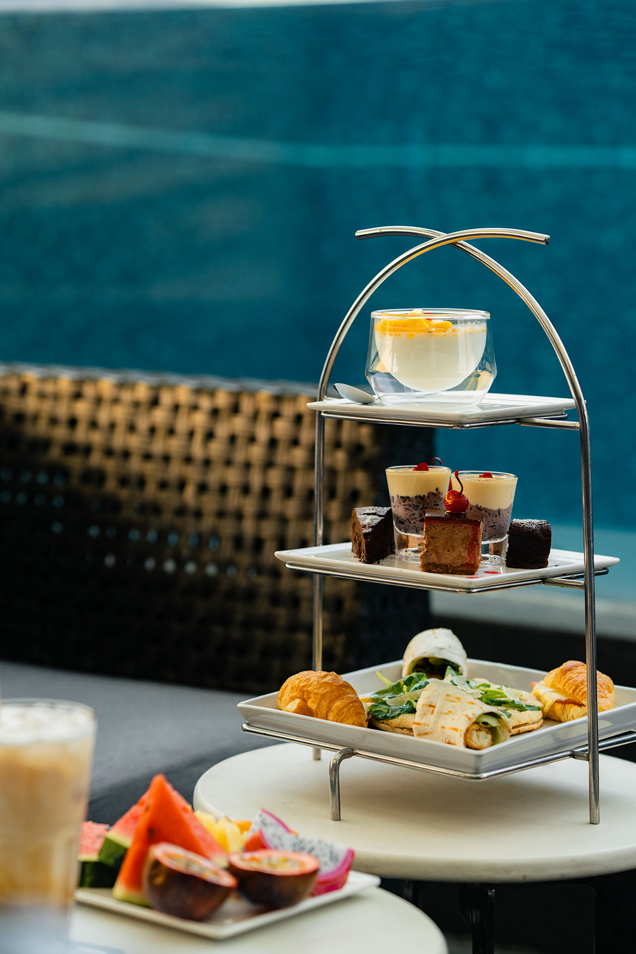 Three-tier afternoon tea stand with pastries, petit fours, and tropical fruit served poolside at Amanor Chiang Mai