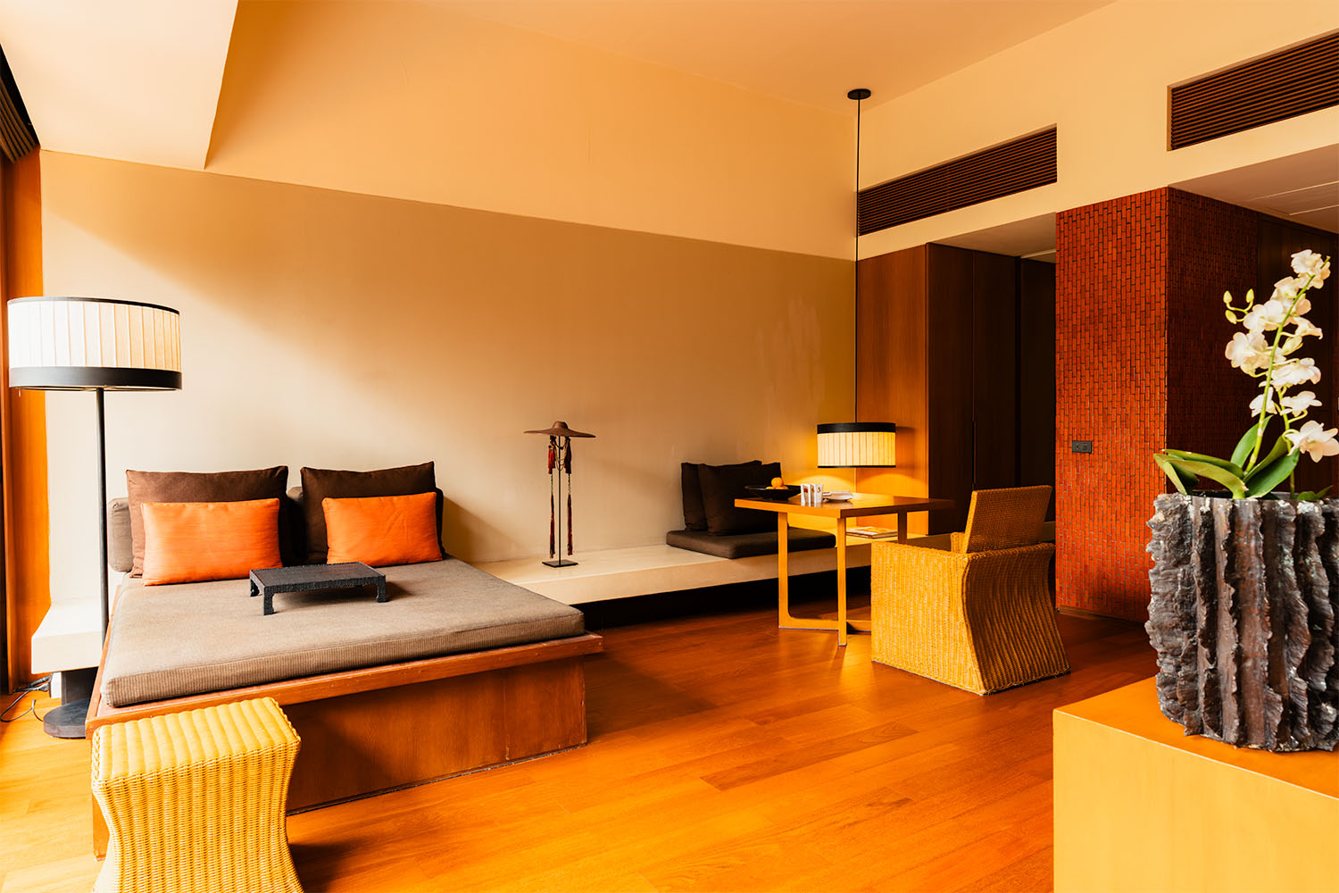 Luxury suite living room at Anantara Chiang Mai with low platform seating, warm timber floors, orange cushions, and orchid arrangement
