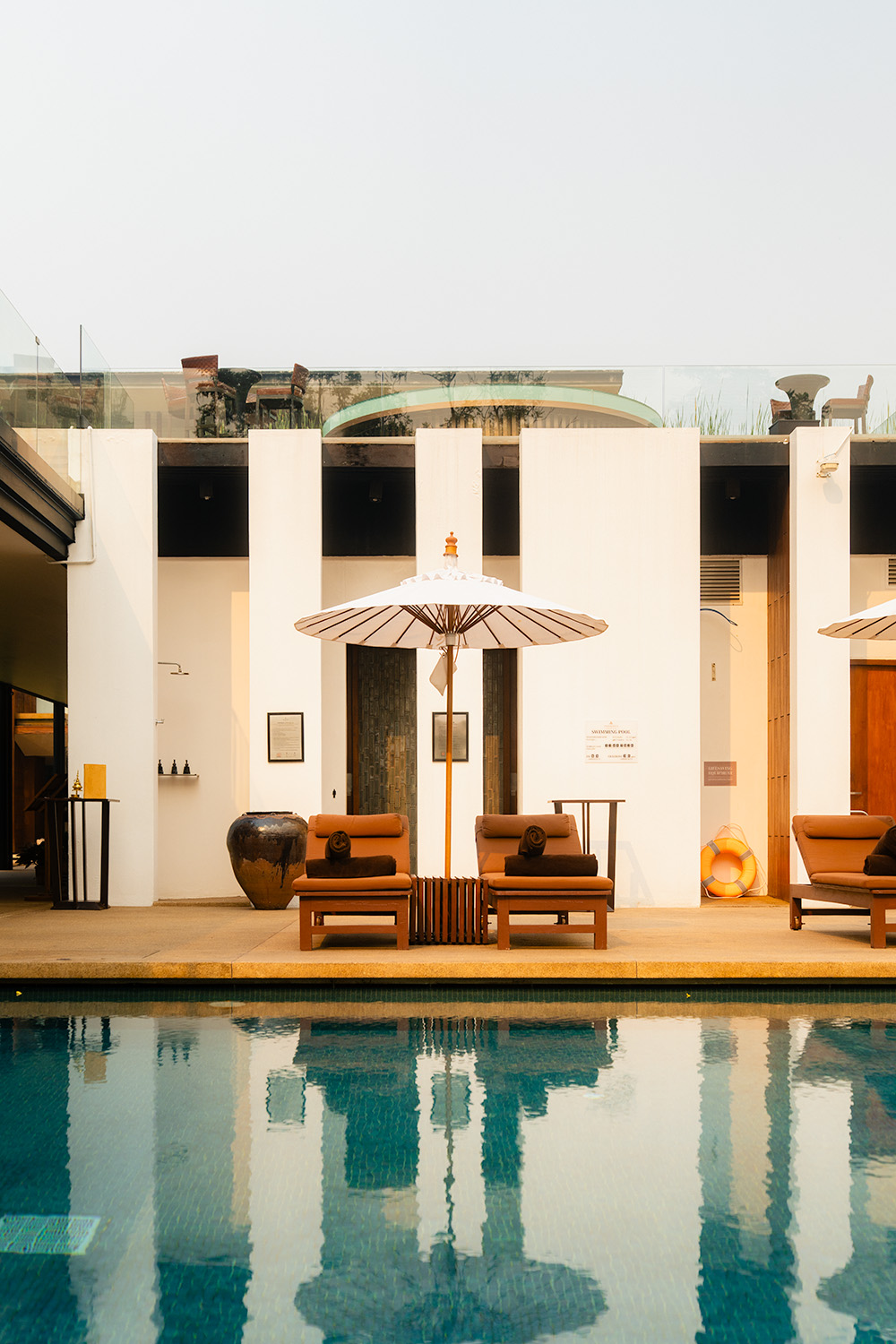 Pool terrace with Thai parasol and wooden sun loungers reflected in still water, Anantara Chiang Mai Resort