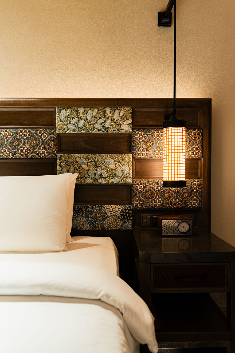 Bedroom detail at Andaz Bali Sanur with dark wood headboard inlaid with Balinese batik fabric panels and woven pendant lamp