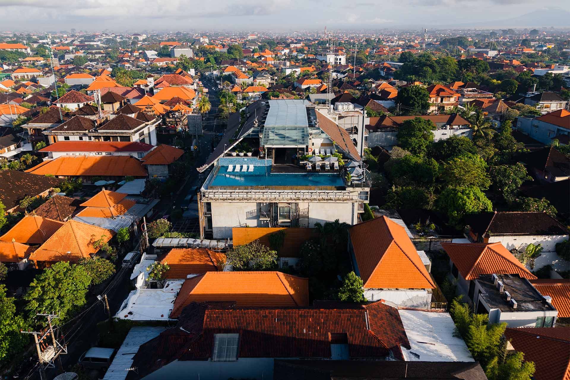 Drone view of ARTOTEL Sanur rooftop infinity pool rising above traditional Balinese orange-tiled rooftops, Sanur, Bali