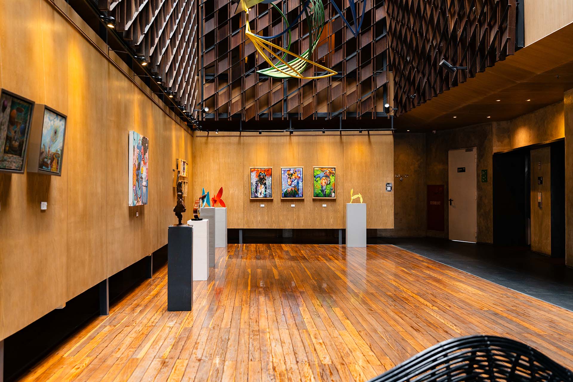 Art gallery lobby at ARTOTEL Sanur Bali with contemporary paintings, sculptural installations, timber floors, and latticed wooden ceiling