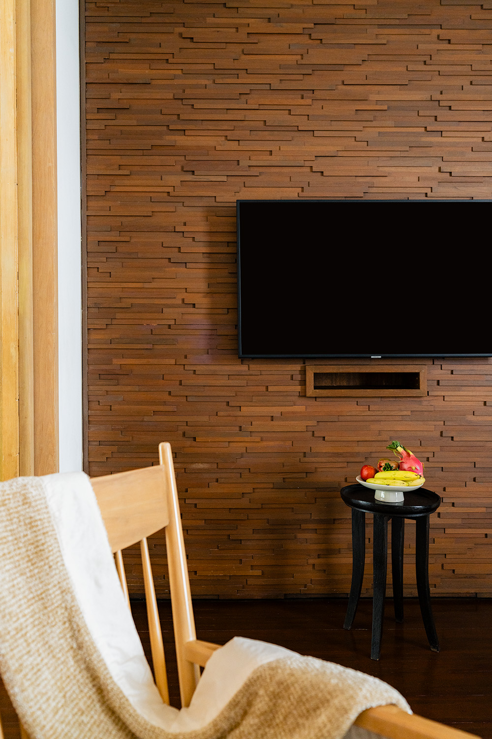 Room interior detail at Grand Hyatt Erawan Bangkok with textured teak wood feature wall, wall-mounted TV, and welcome fruit bowl