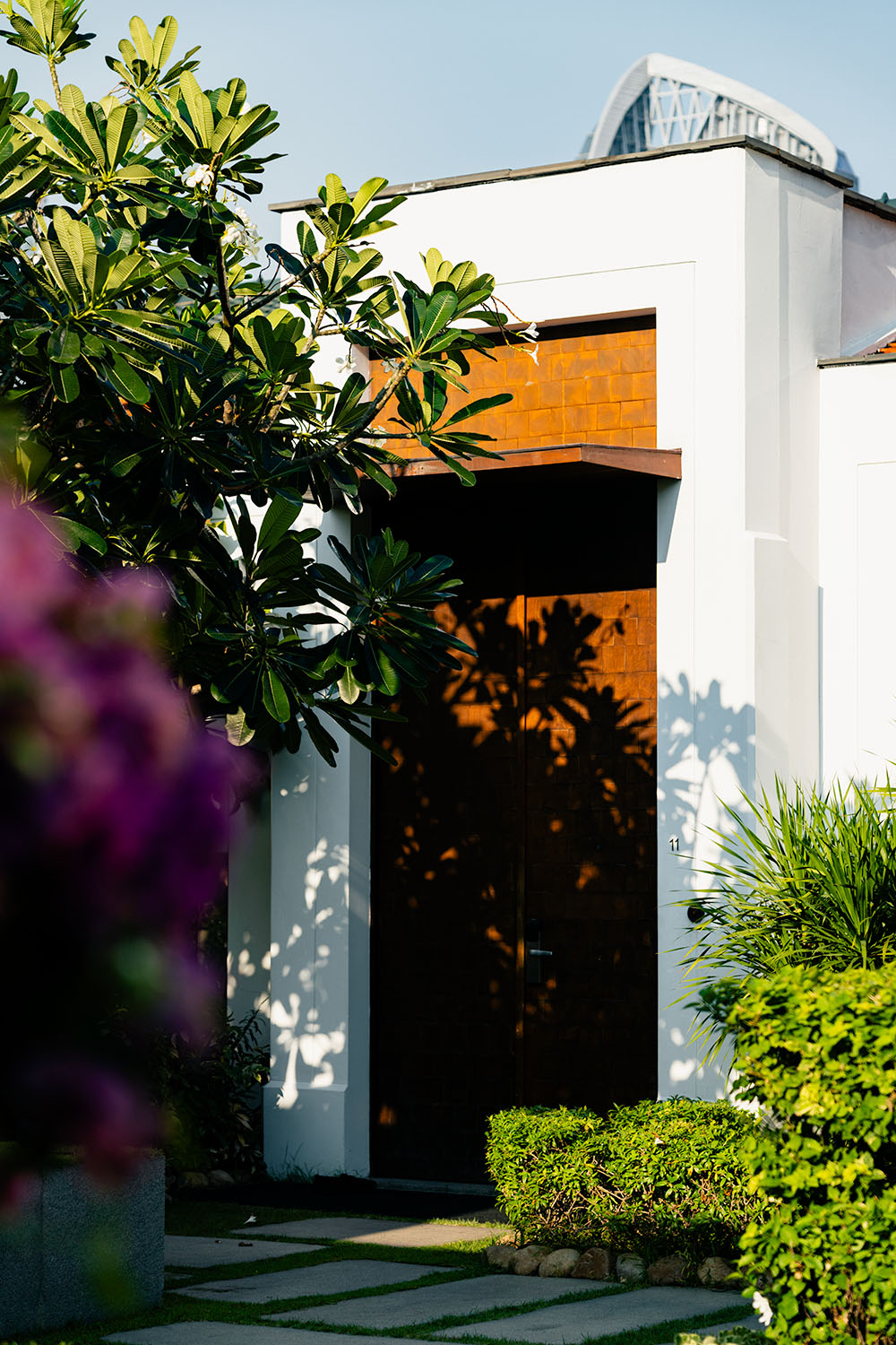 Private villa entrance at Grand Hyatt Erawan Bangkok with terracotta tile facade, frangipani trees, and dappled afternoon shadows