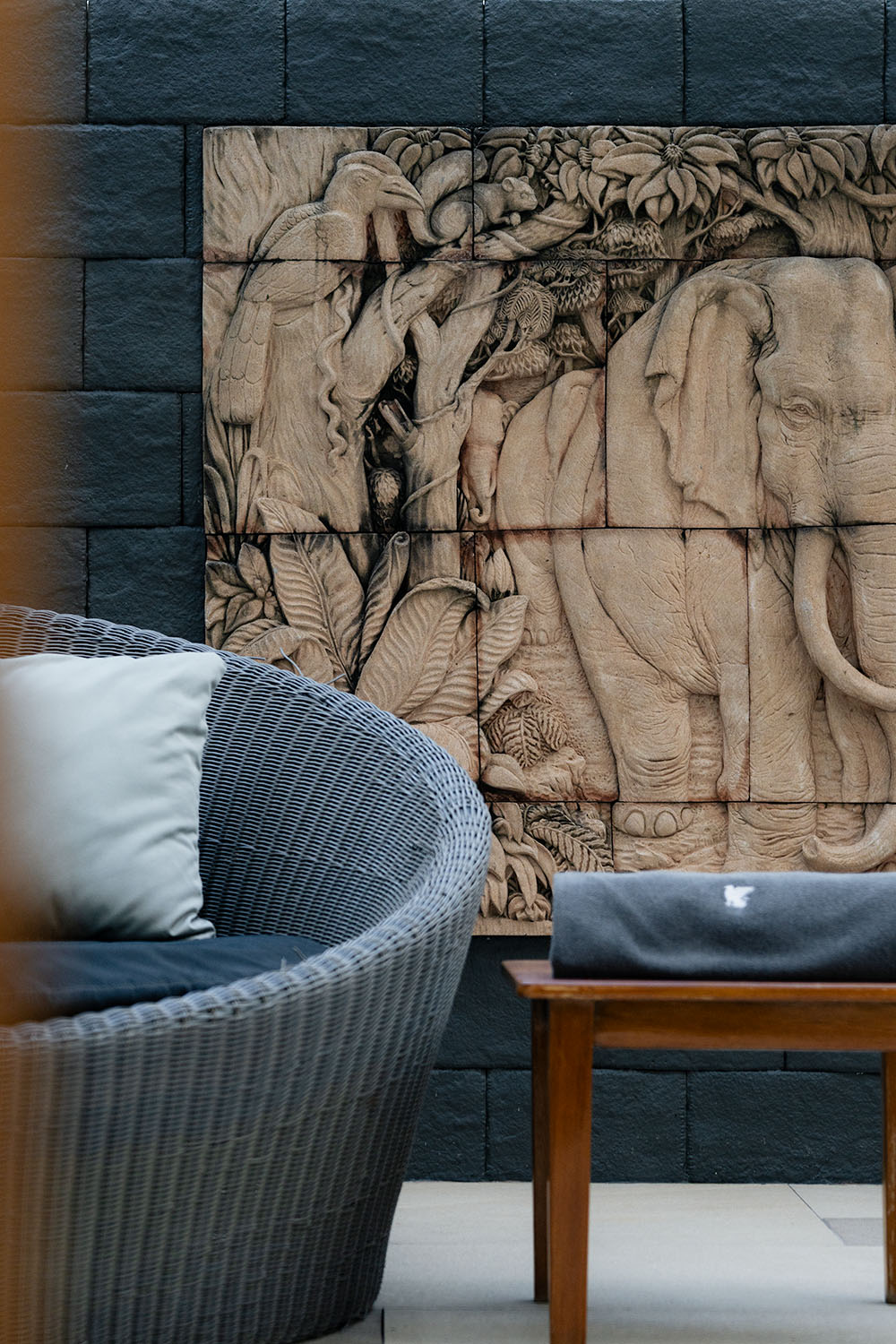Stone-carved elephant relief artwork on slate wall with wicker lounge chair, JW Marriott Bangkok