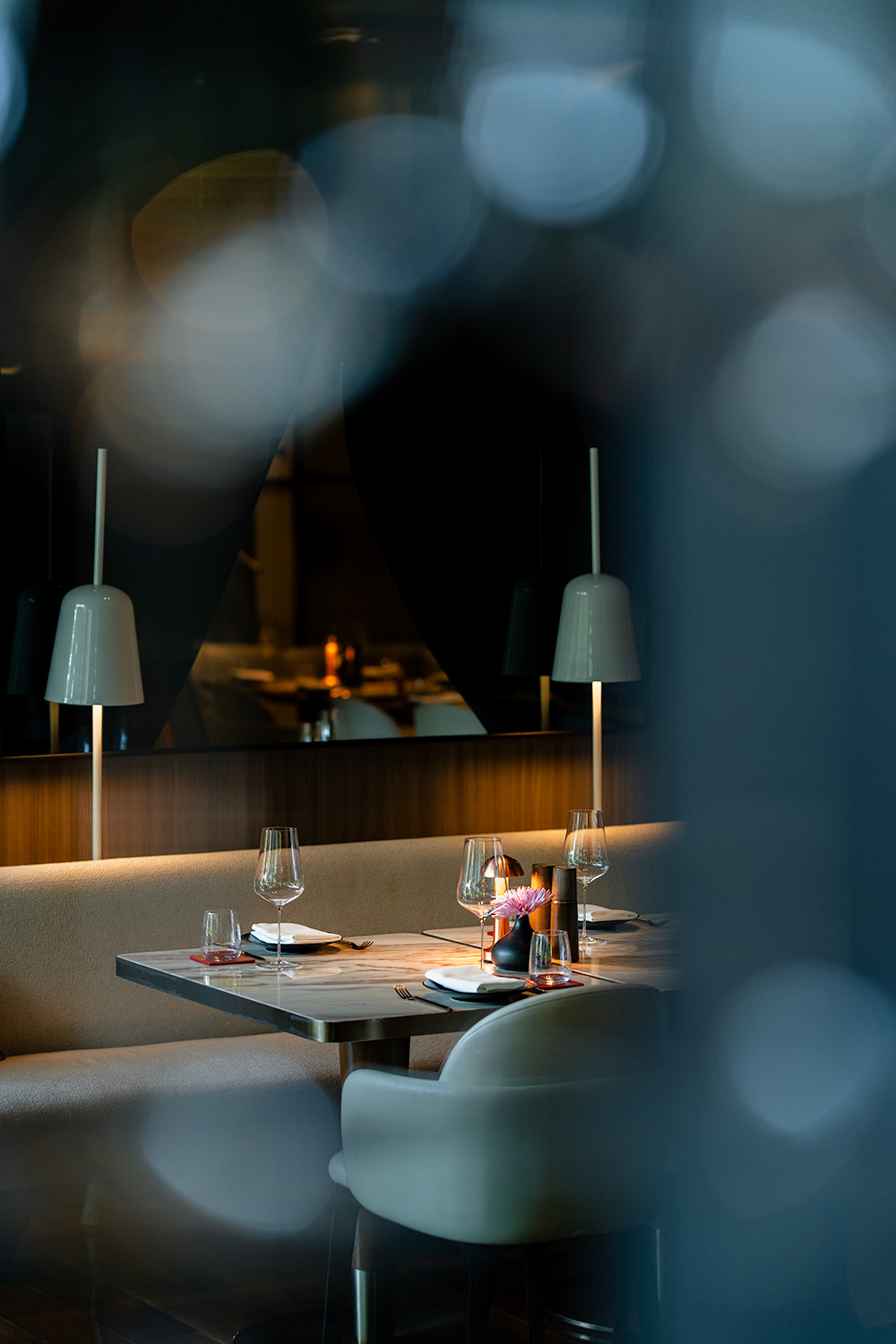 Intimate restaurant table set for dinner seen through soft bokeh foreground, Kimpton Maa-Lai Bangkok