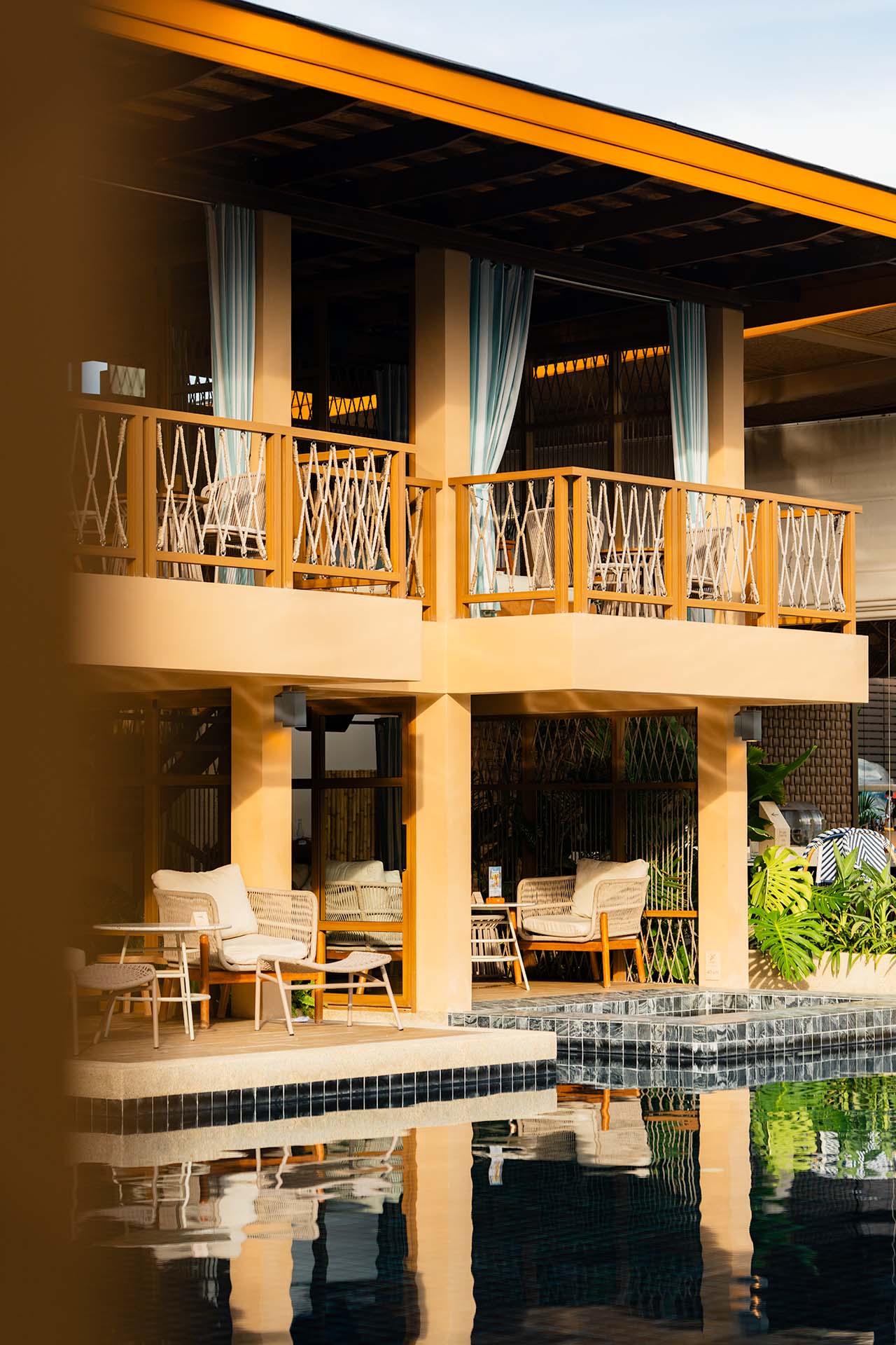 Marasca Koh Samui pool terrace at golden hour with rattan seating, rope-railed balconies, and dark tiled pool reflection — Small Luxury Hotels