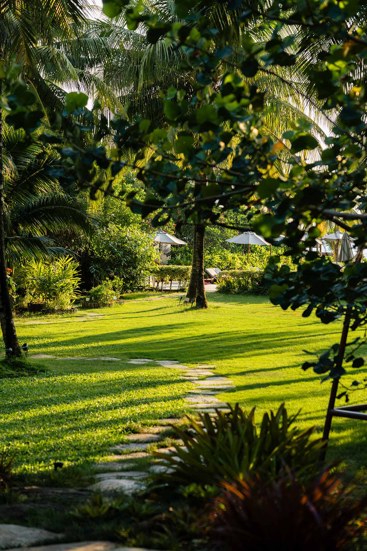 Stone pathway through lush tropical garden leading to beachside sun loungers and parasols at The Retreat Koh Chang
