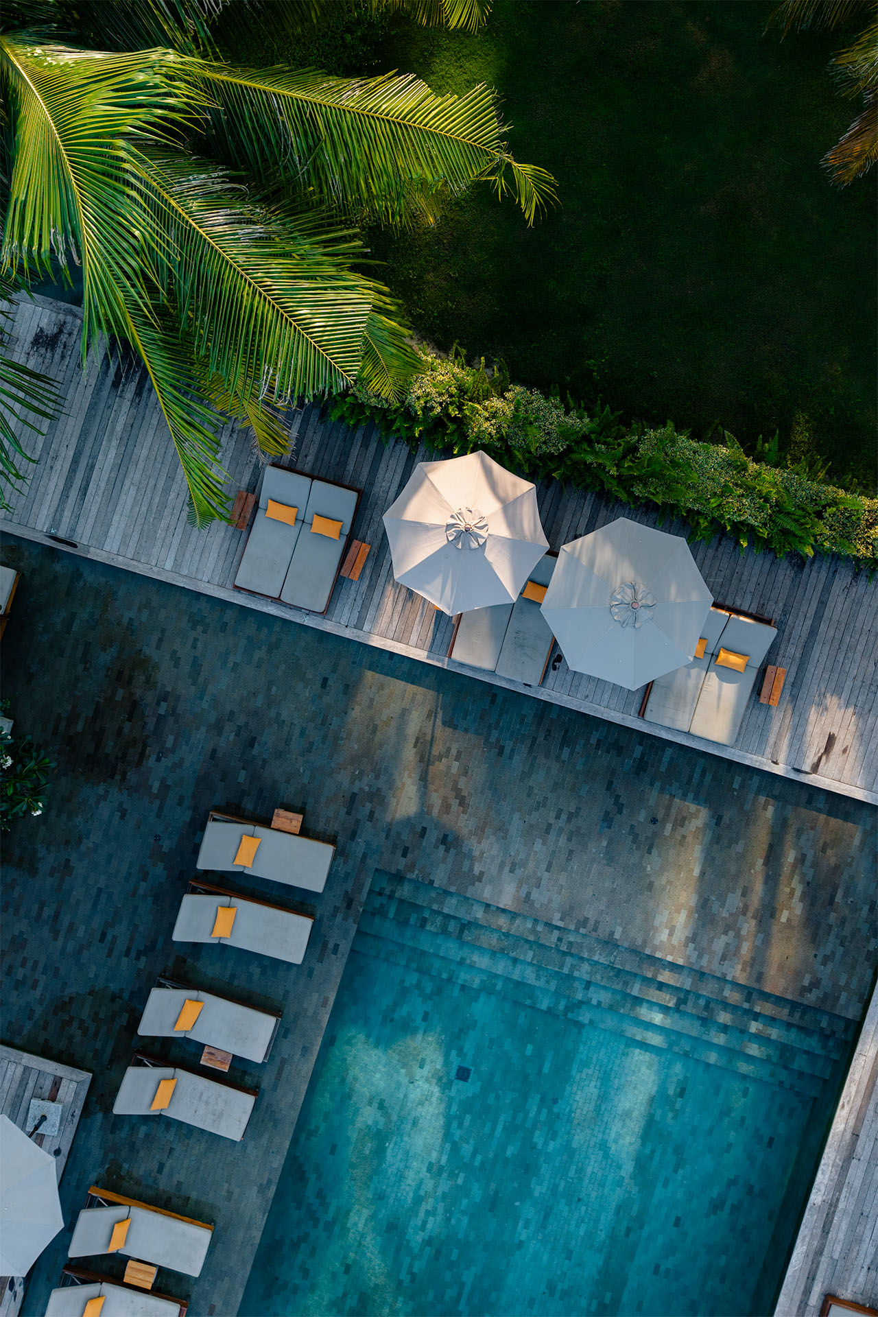 Aerial top-down view of The Retreat Koh Chang pool deck with grey sun loungers, yellow cushions, and parasols amid tropical foliage