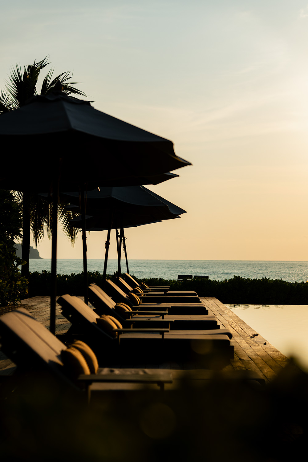 Sun loungers and parasols silhouetted against a golden ocean sunset at The Retreat Koh Chang infinity pool